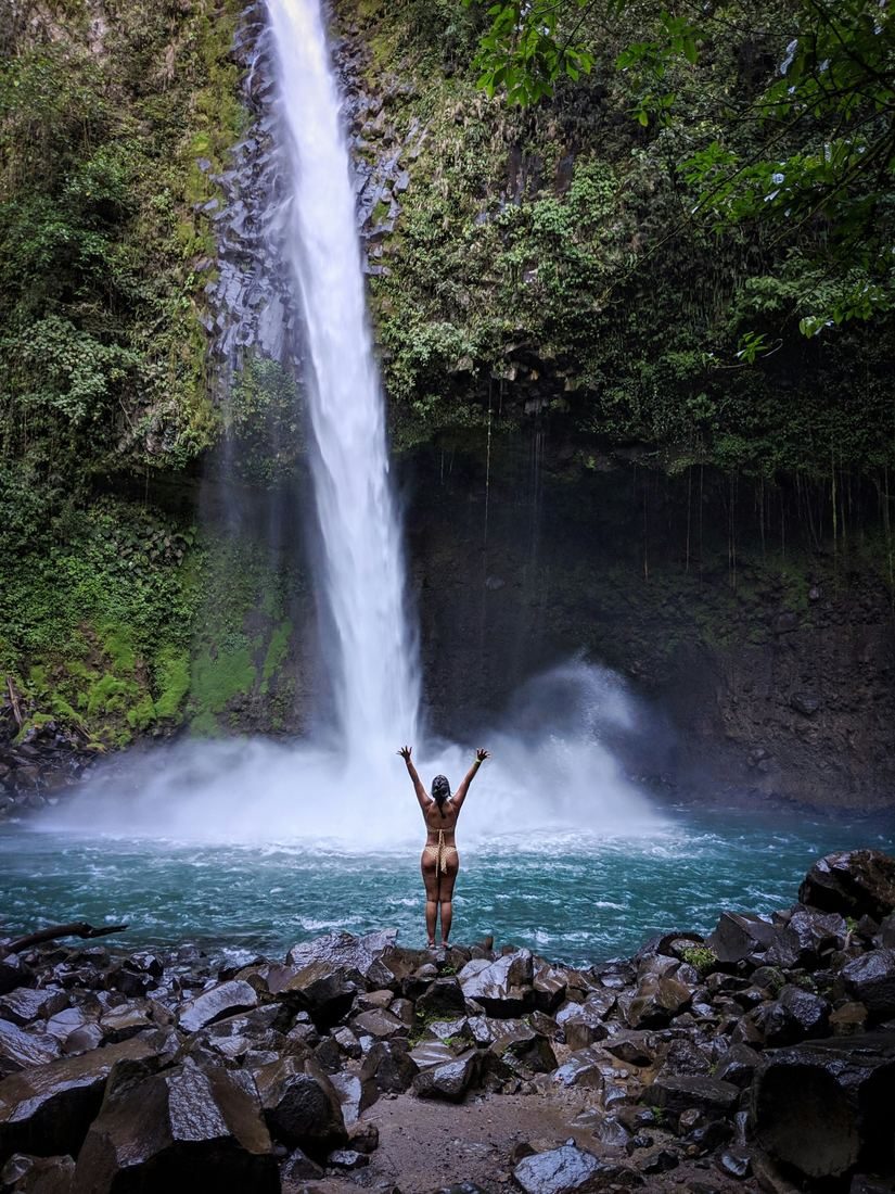 Woman with arms raised in front of La Fortuna Waterfall