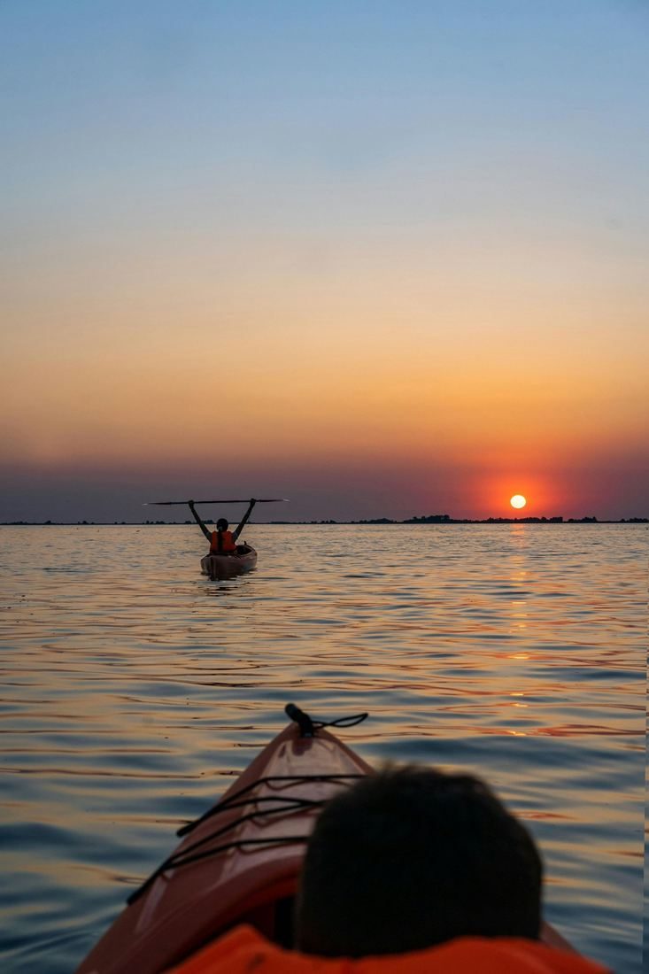 Kayaker raising her paddle at sunset on calm water